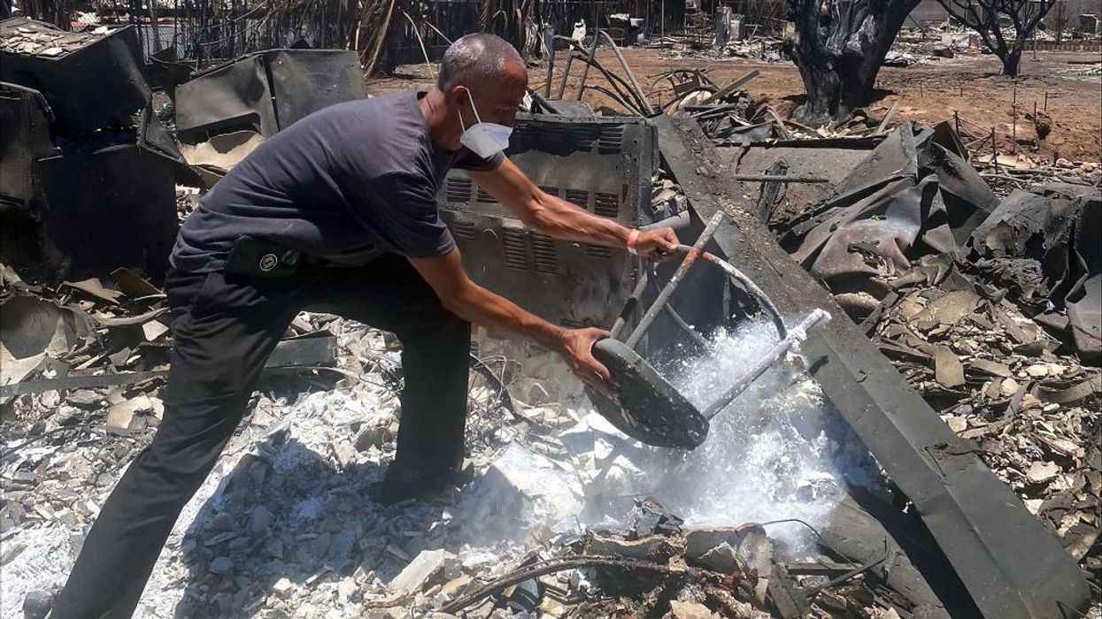 A man in a face mask removes items from the ashes of his home.
