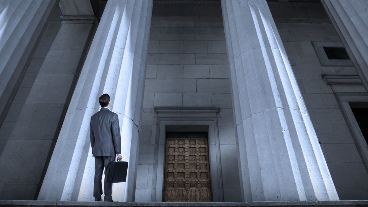 A man in a suit with a briefcase looks up at a courthouse. 