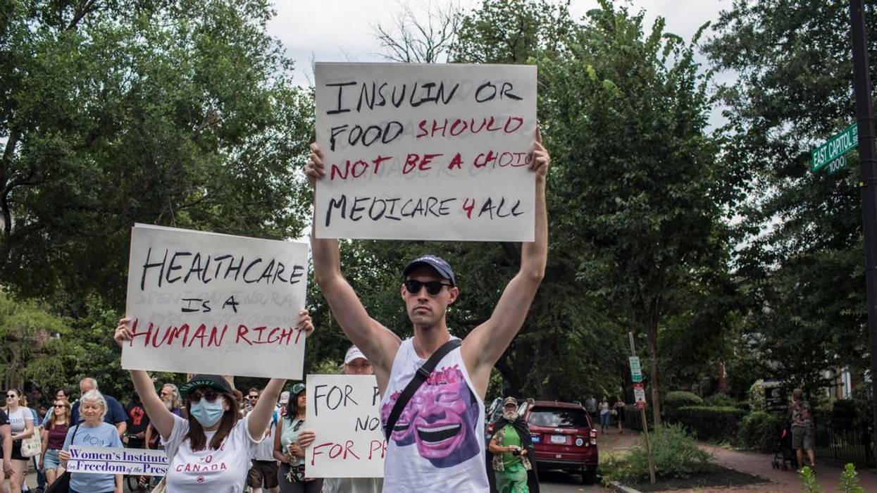 A man in a tank top holds up a sign reading, "Insulin or food should not be a choice. Medicare 4 All."