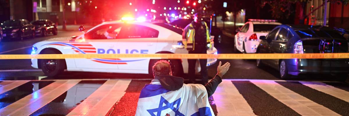 A man in an Israeli flag stands in front of a police line and car.