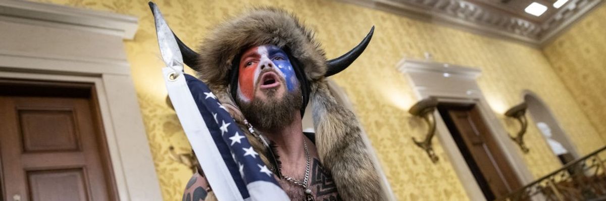 A man in red-white-and-blue face paint and horns yells in the U.S. Senate chamber.