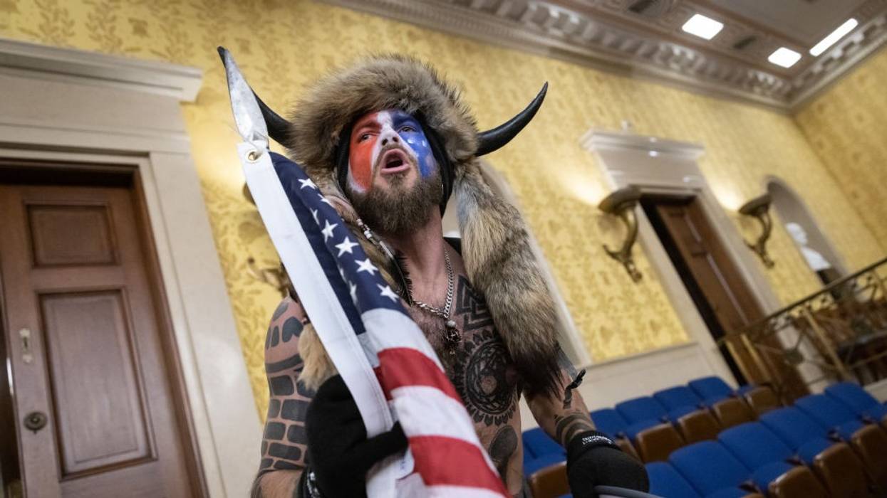 A man in red-white-and-blue face paint and horns yells in the U.S. Senate chamber.