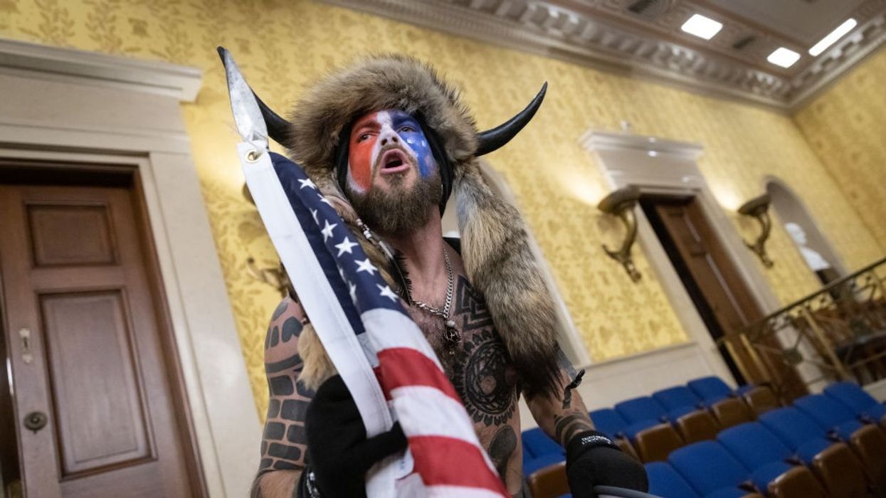 A man in red-white-and-blue face paint and horns yells in the U.S. Senate chamber.