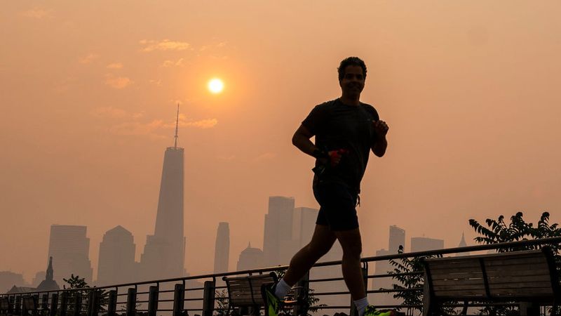 A man jogs in wildfire smoke with NYC in the background.