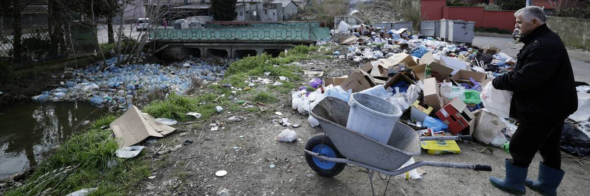 A man looks for goods to retrieve in a dumping area near plastic trash-filled floodwaters
