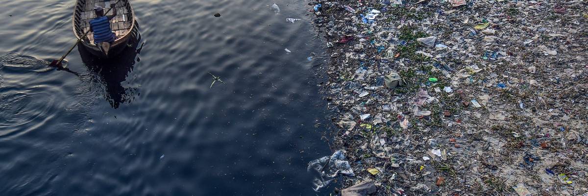 A man paddles on a boat as plastic bags float on the surface of the Buriganga River in Dhaka, Bangladesh on January 21, 2020.