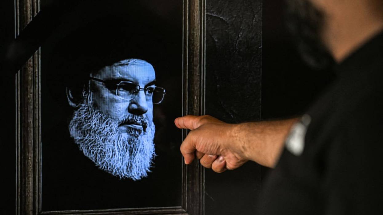A man points to a television set displaying an image of the late leader of Hezbollah Hassan Nasrallah