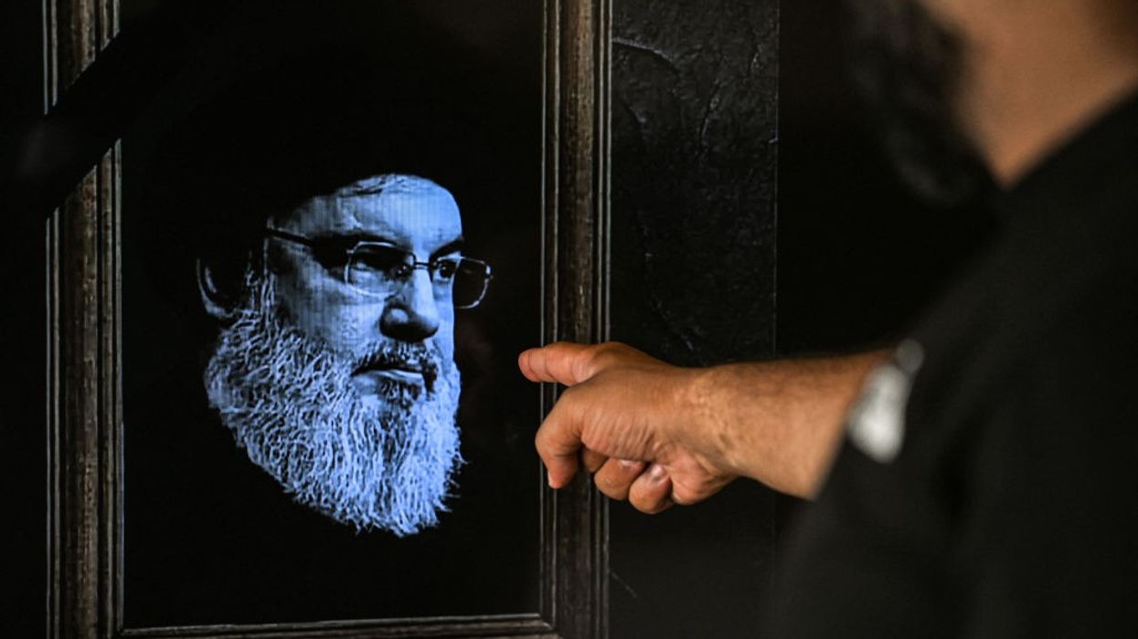 A man points to a television set displaying an image of the late leader of Hezbollah Hassan Nasrallah