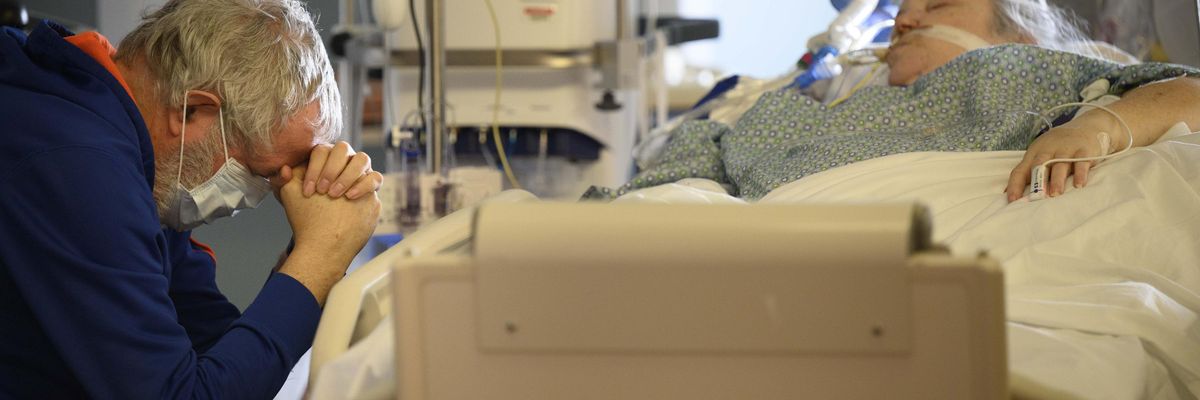 A man prays at the bedside of his critically ill wife