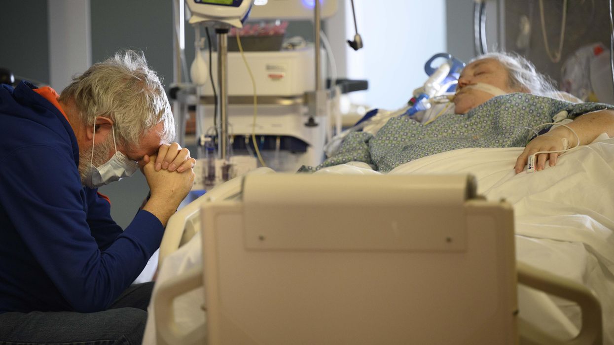 A man prays at the bedside of his critically ill wife