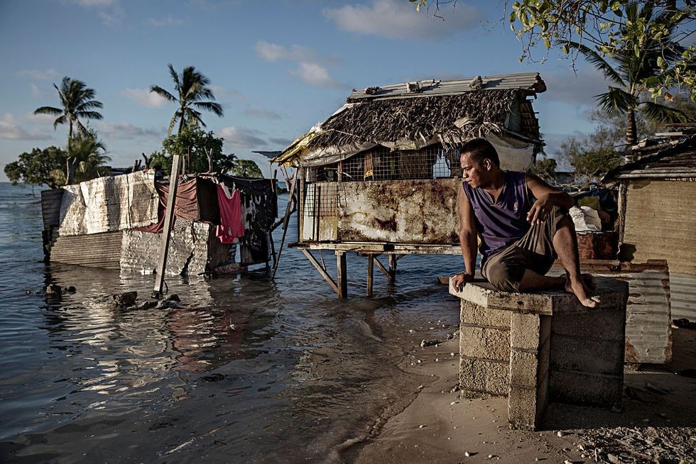 A man sits on a stone pillar and looks at encroaching sea water.