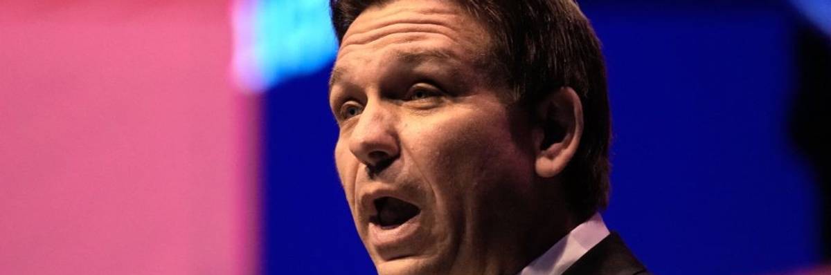 A man speaks against a pink and blue background.