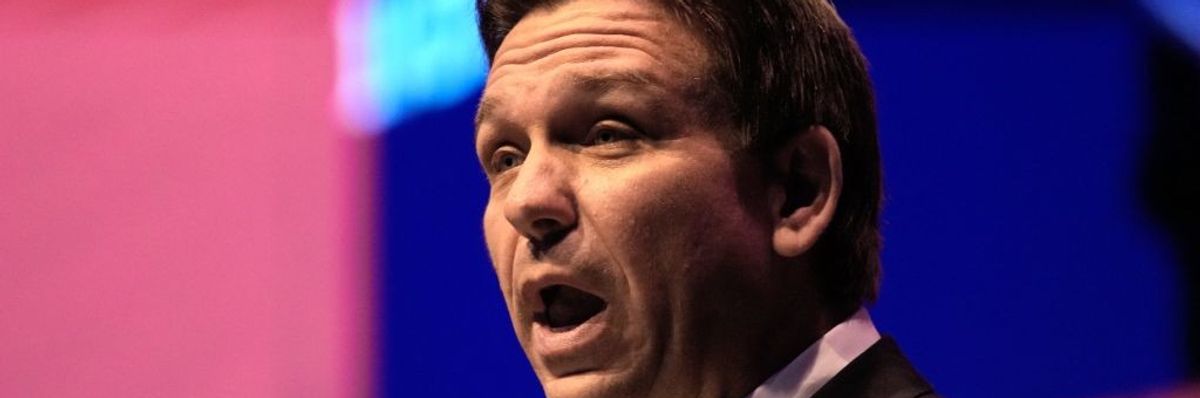 A man speaks against a pink and blue background.