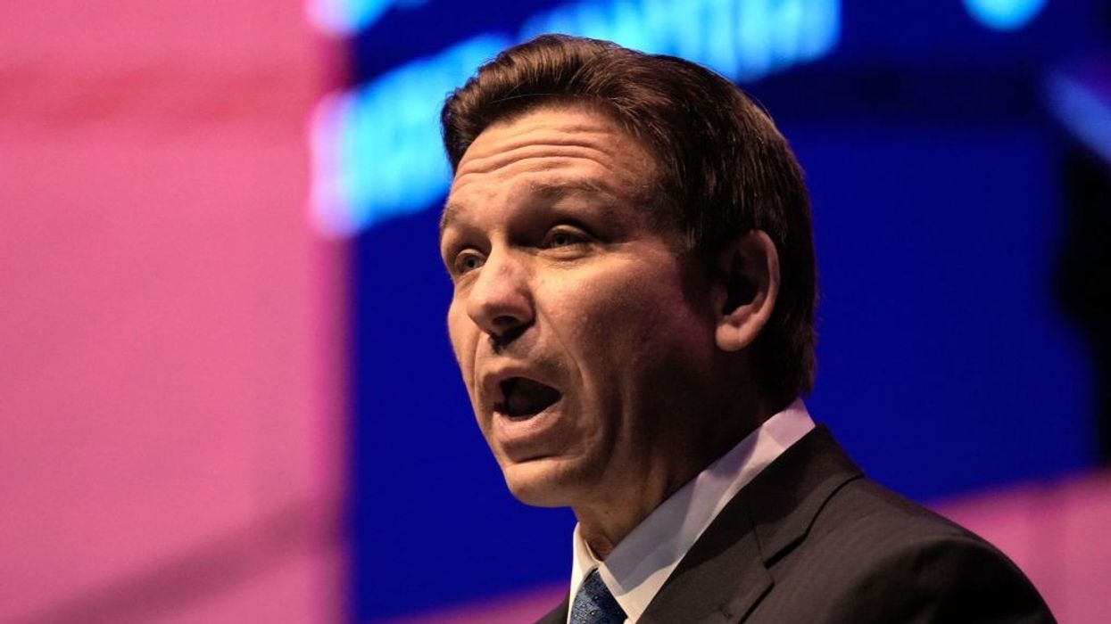 A man speaks against a pink and blue background.
