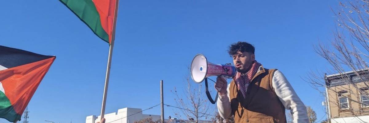 A man speaks into a bullhorn as Palestinian flags wave in the air.