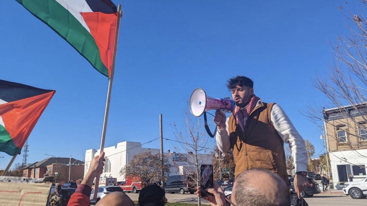 A man speaks into a bullhorn as Palestinian flags wave in the air.