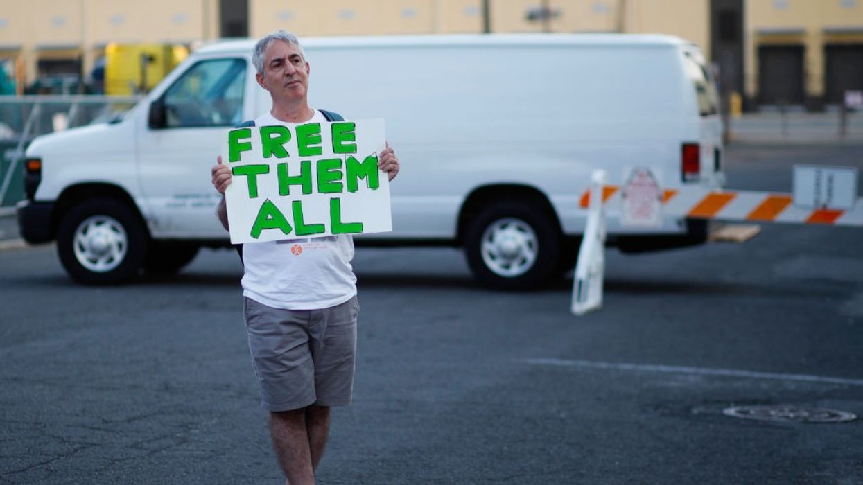 A man stands in front of a white van with a white sign reading, "Free them all," in green.