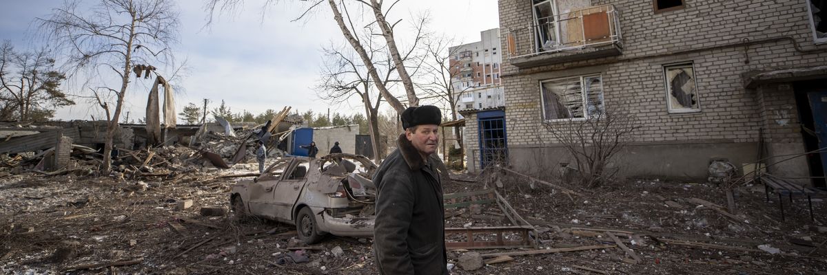 A man stands near a damaged vehicle and building in Lyman, Ukraine on February 13, 2023, nearly a year into Russia's invasion.