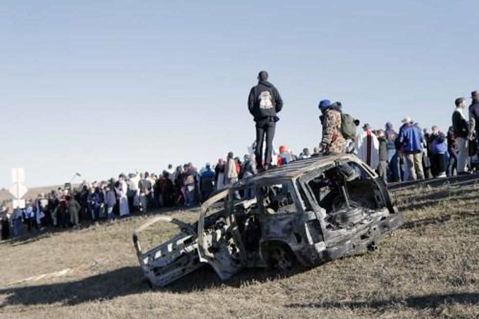 A man stands on a burnt-out SUV as interfaith witnesses share testimony and commit to carrying with them home the message from Standing Rock.