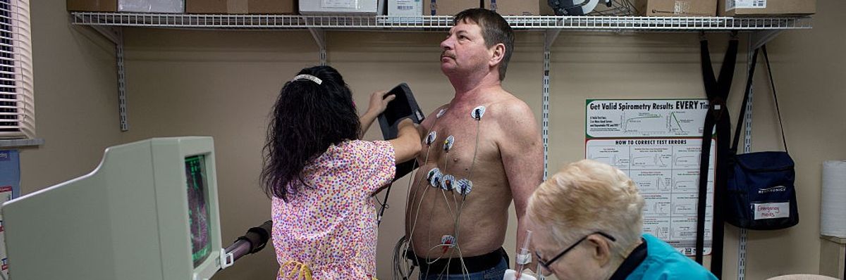 A man stands with electrodes on his chest as a doctor examines him.