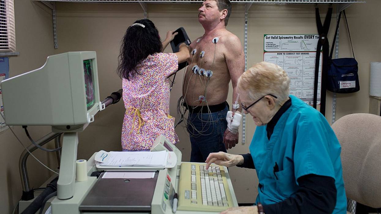A man stands with electrodes on his chest as a doctor examines him.