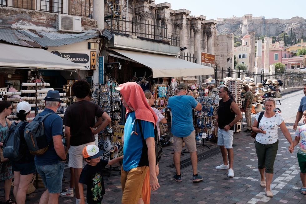 A man wears a red towel on his head in a crowded street in Greece.