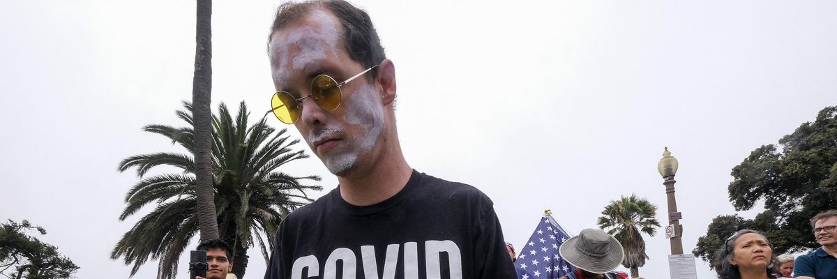 A man wears a shirt saying "Covid is a scam"