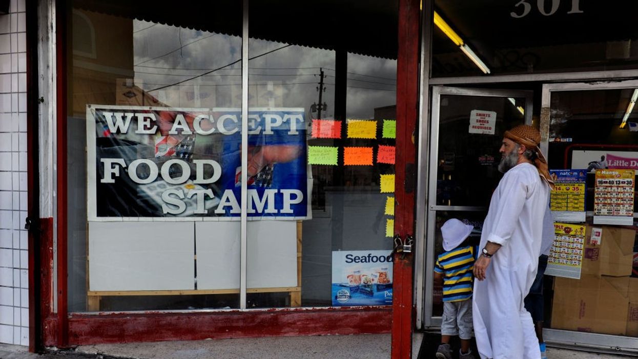 A man with a gray beard looks at a sign reading, "We accept food stamps."