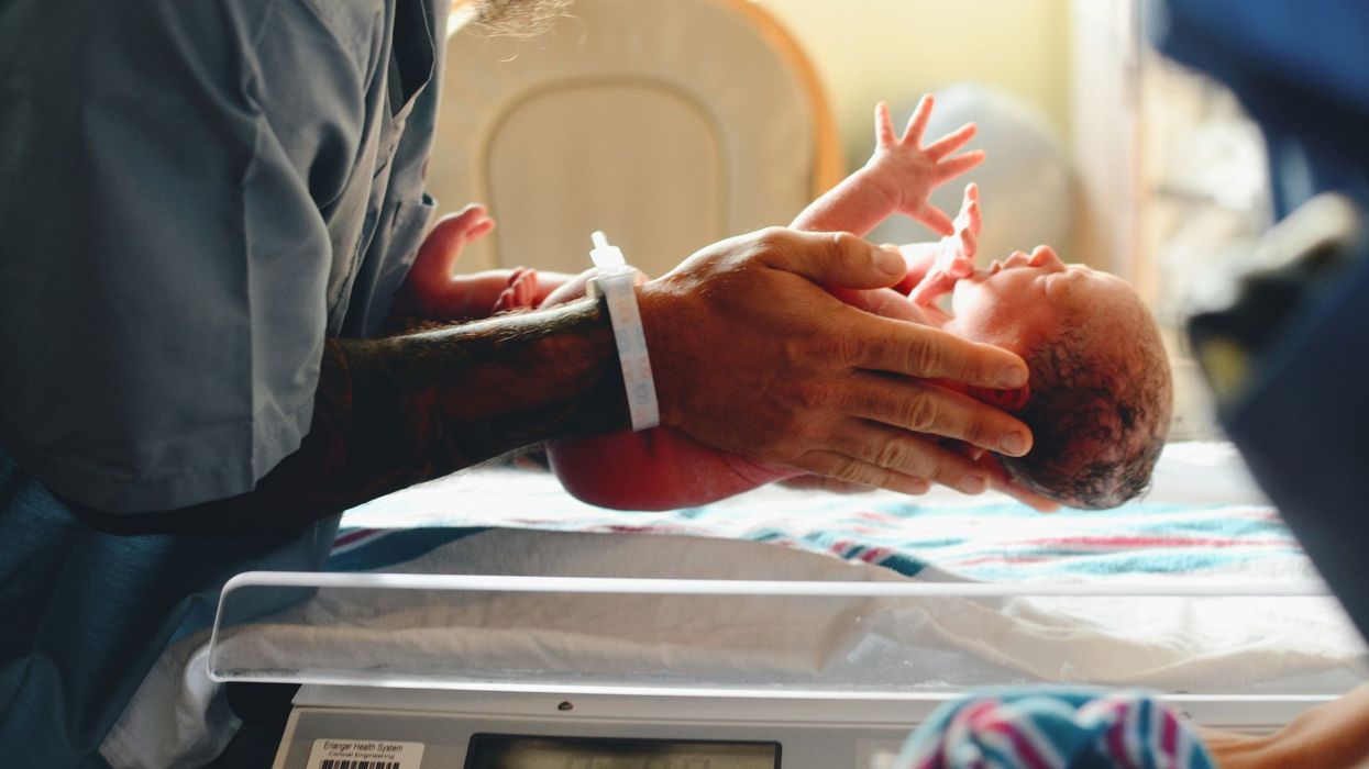 A medical worker is seen putting a newborn baby on a scale.