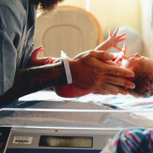 A medical worker is seen putting a newborn baby on a scale.