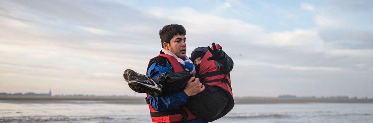 A migrant carries a child as he runs to board a smuggler's boat on the beach in France