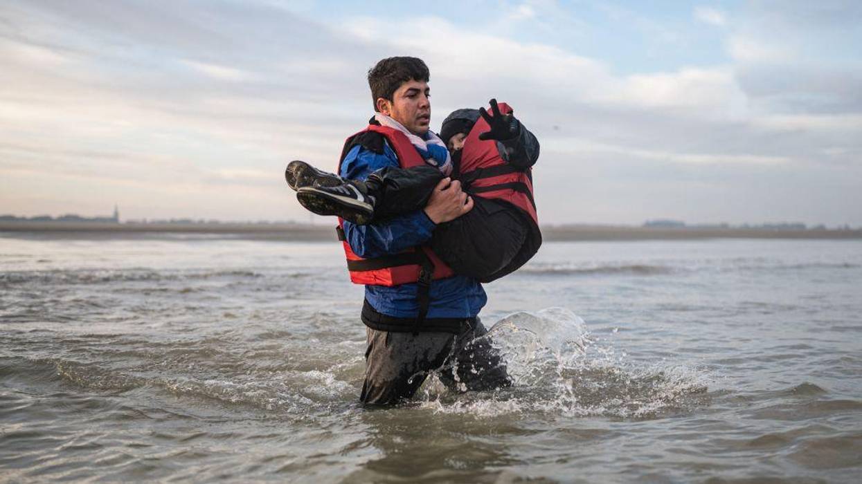 A migrant carries a child as he runs to board a smuggler's boat on the beach in France