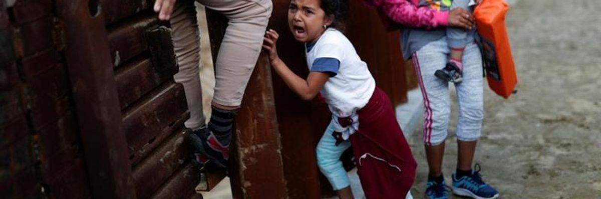 A migrant girl from Central America cries next to the border wall 