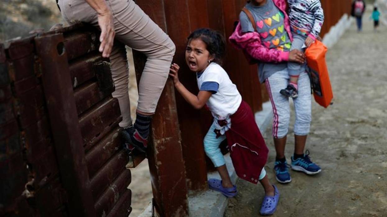 A migrant girl from Central America cries next to the border wall