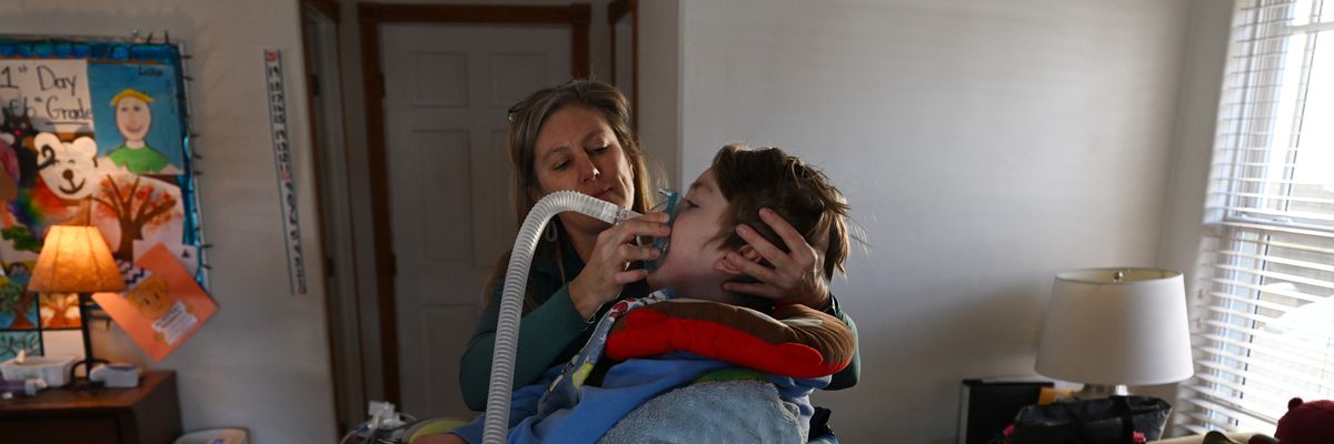 A mother helps her 12-year-old son with a breathing treatment