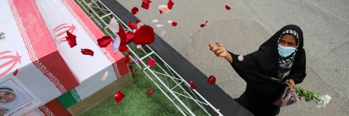 A mourner throws rose petals on the coffins of children killed in Iran.