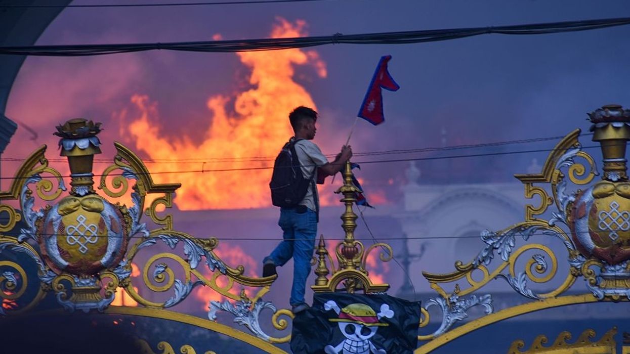 A Nepalese protester holds a flag as a government building burns in the background