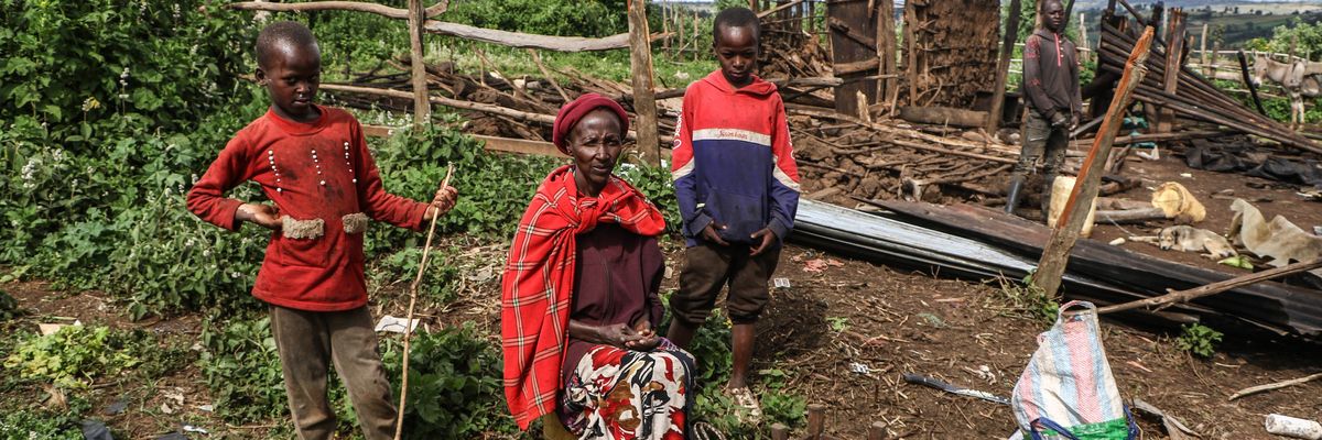 A Ogiek woman sits amid the ruins of her demolished home with her children on either side.