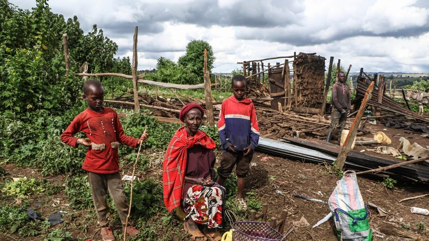A Ogiek woman sits amid the ruins of her demolished home with her children on either side.