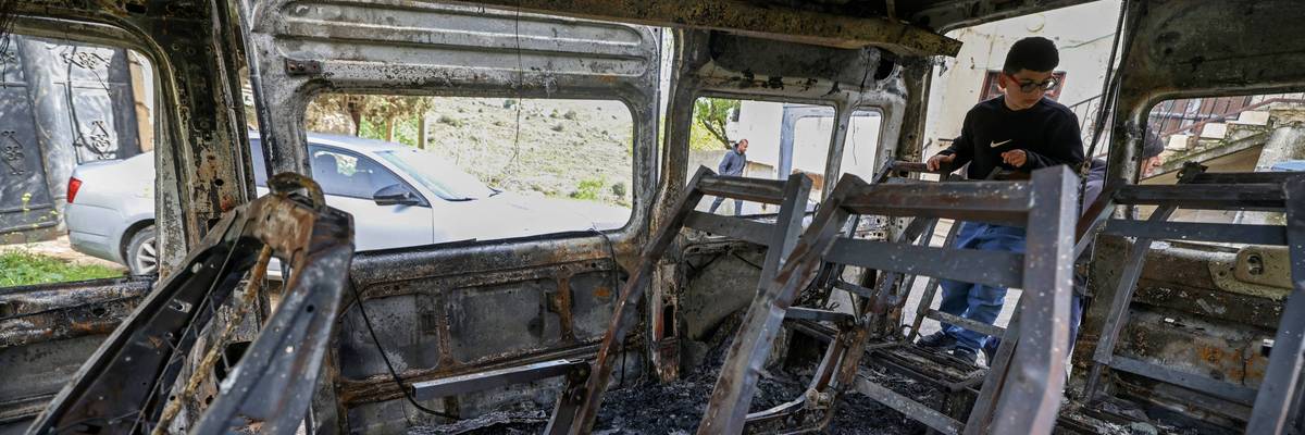 A Palestinian boy looks at a burnt vehicle in the West Bank.