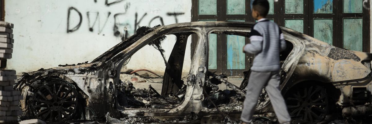 A Palestinian boy walks near a burned car