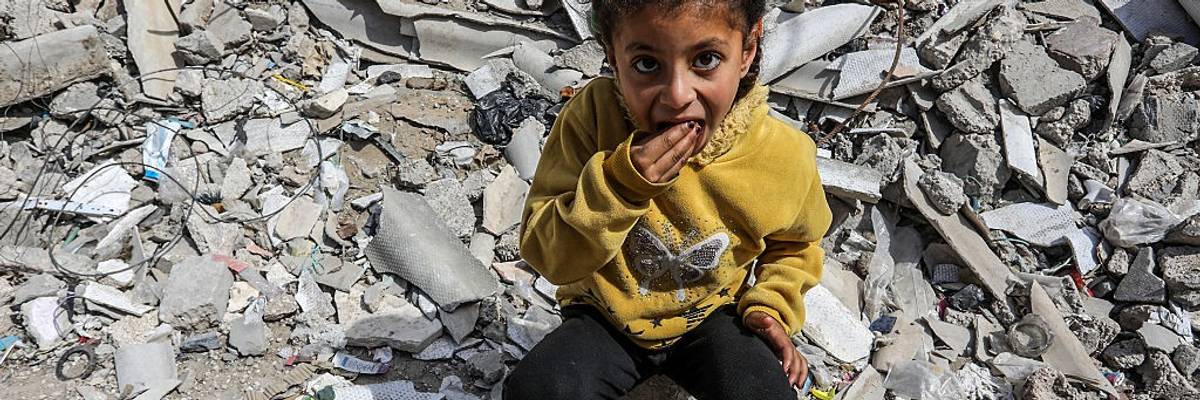 A Palestinian girl eats from a pot of rice amid the rubble of Gaza