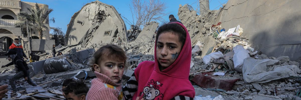 A Palestinian girl holds a child on rubble