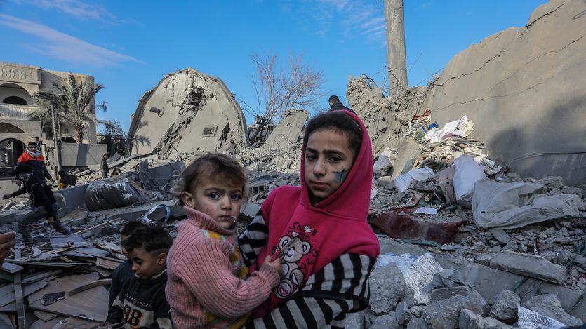 A Palestinian girl holds a child on rubble