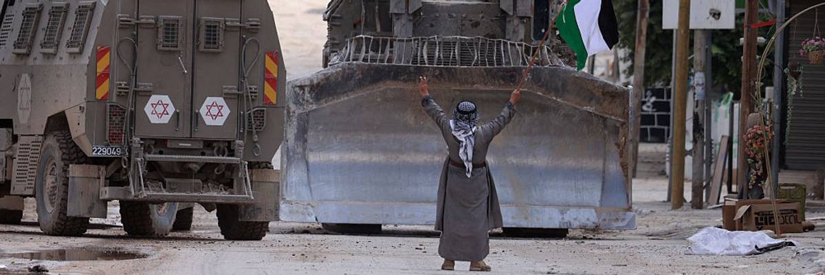 A Palestinian holding a flag blocks an Israeli bulldozer