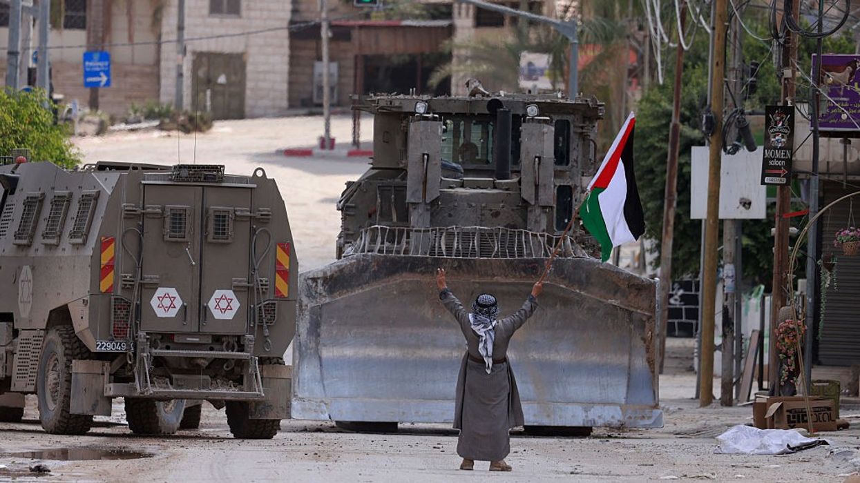 A Palestinian holding a flag blocks an Israeli bulldozer