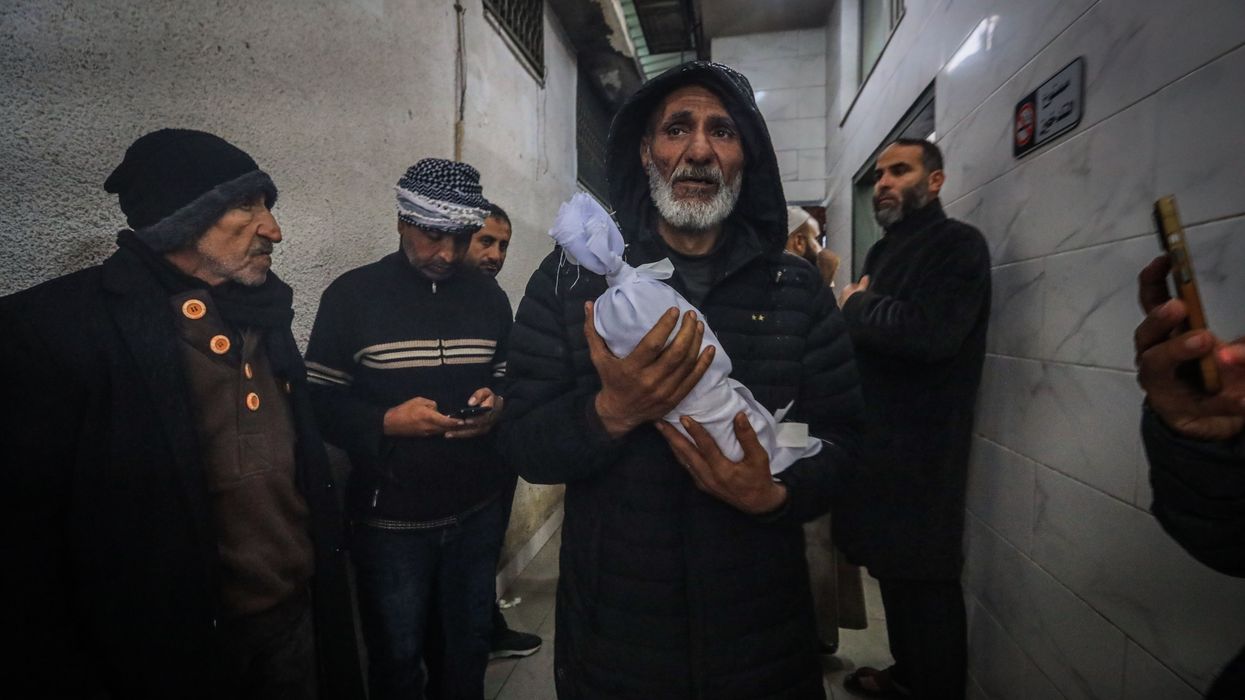 A Palestinian man carried the shrouded body of an infant who died of exposure in Gaza