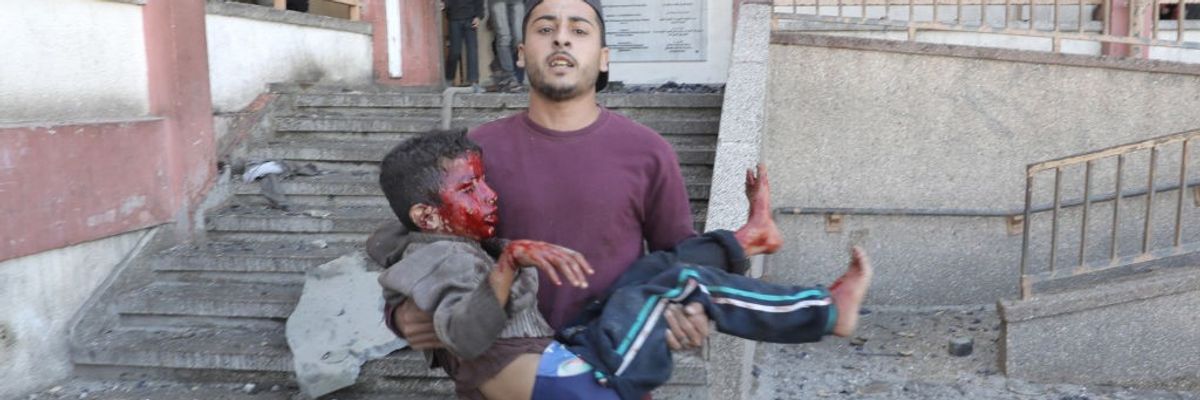 A Palestinian man carries a child, his face bloodied after being injured by an Israeli strike