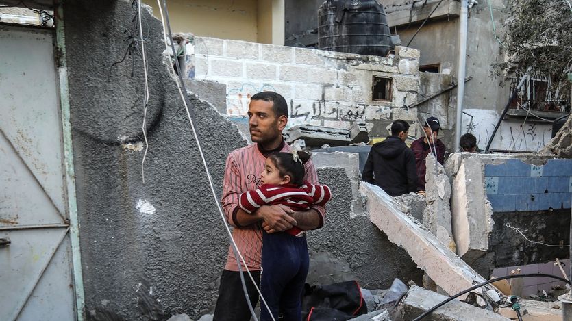 A Palestinian man consoles a girl near a damaged building
