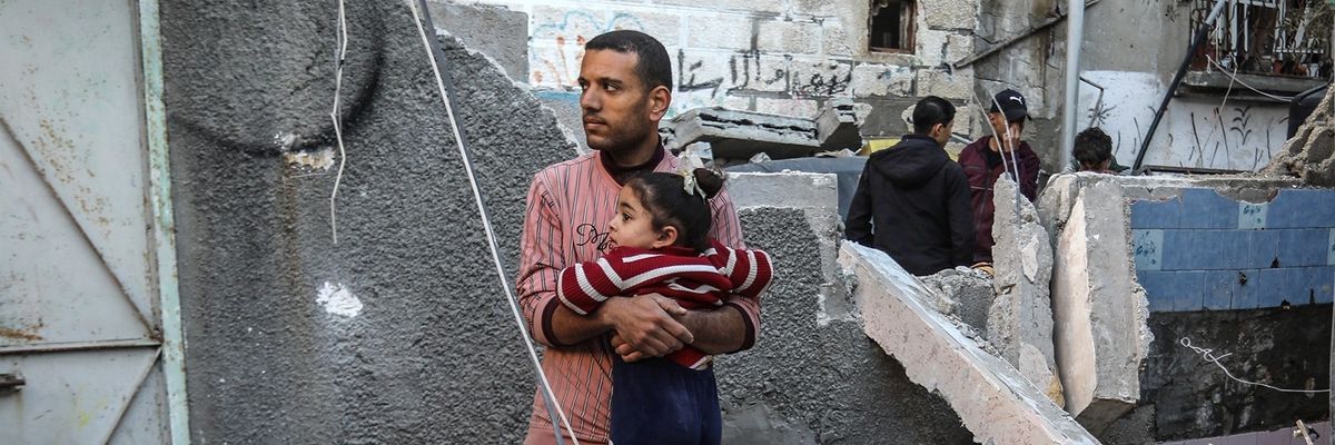 A Palestinian man consoles a girl near a damaged building